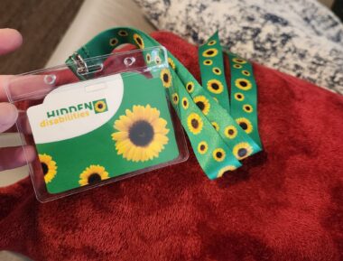 A green lanyard with sunflowers on it is connected to a tag that reads "Hidden Disabilities."