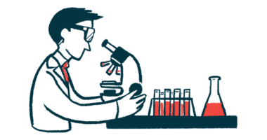 A researcher looks into microscope that's sitting next to a rack of filled test tubes and a beaker.