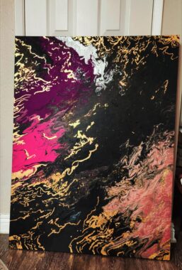 A large abstract painting sits on the floor - it's a wave of colors ranging from charcoal to purple to pink. Gold streaks highlight it throughout the piece. 